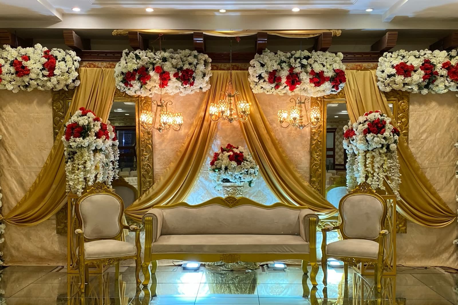 A wedding stage at Naulakha, with gold drapes, crystal chandeliers and red and white flowers