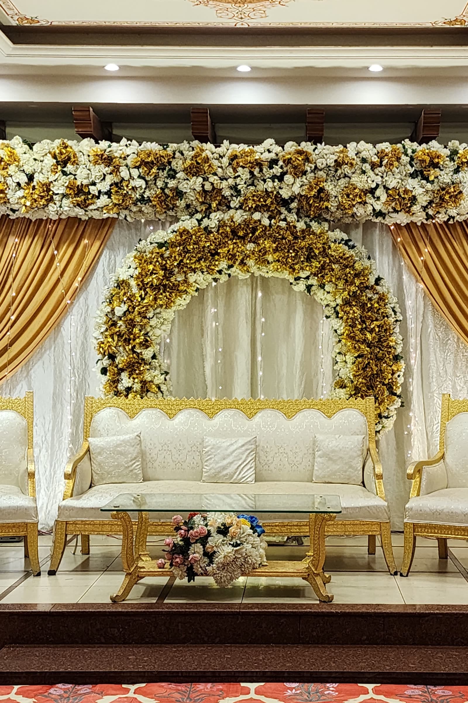 A wedding stage at Naulakha, with gold drapes and a white and gold flower arch