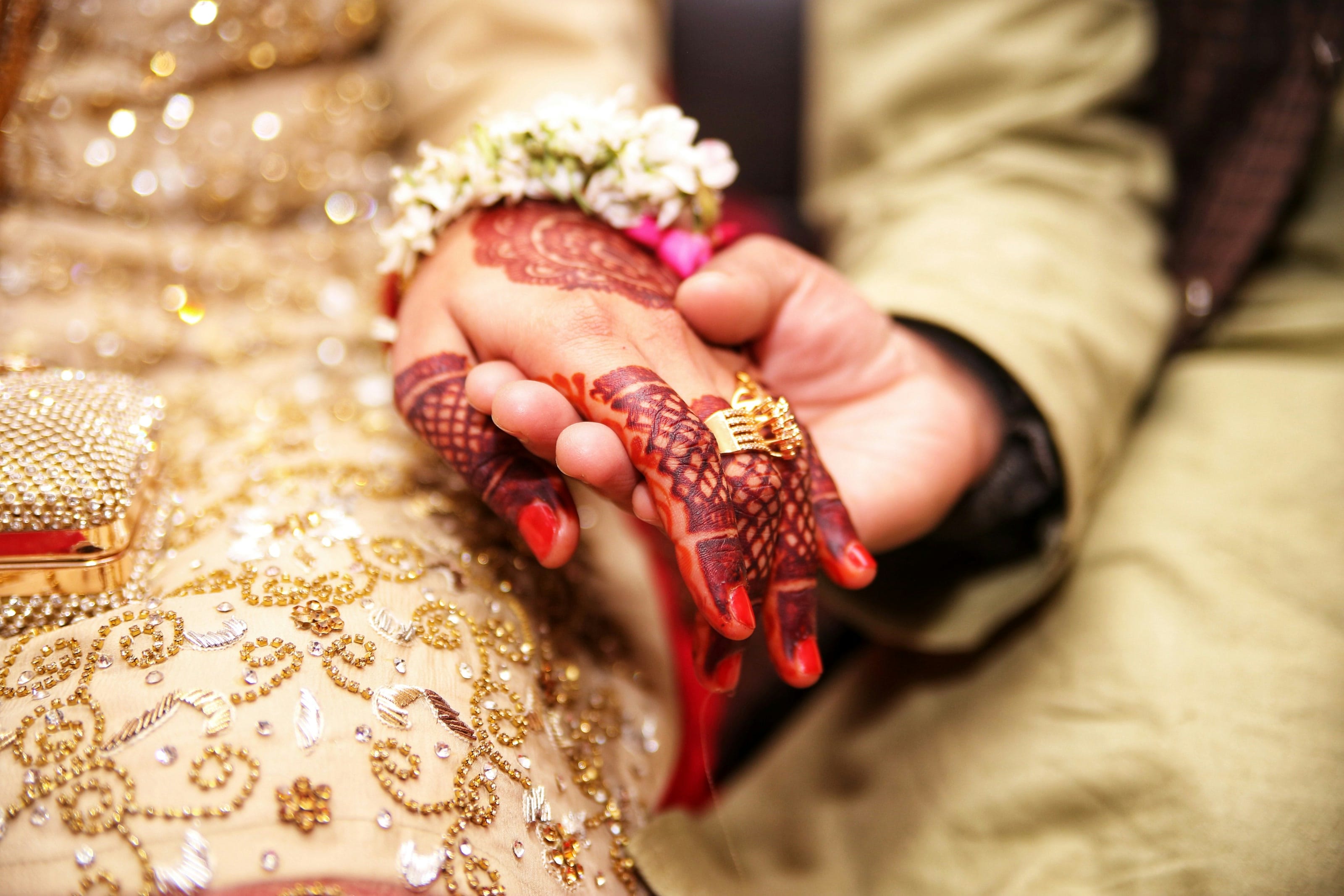 A bride's hand with henna and a gold ring, held by the groom